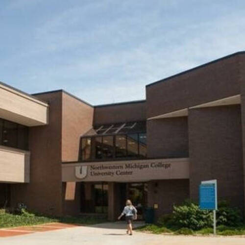 Two-story brown brick academic building with large windows and landscaped entrance.